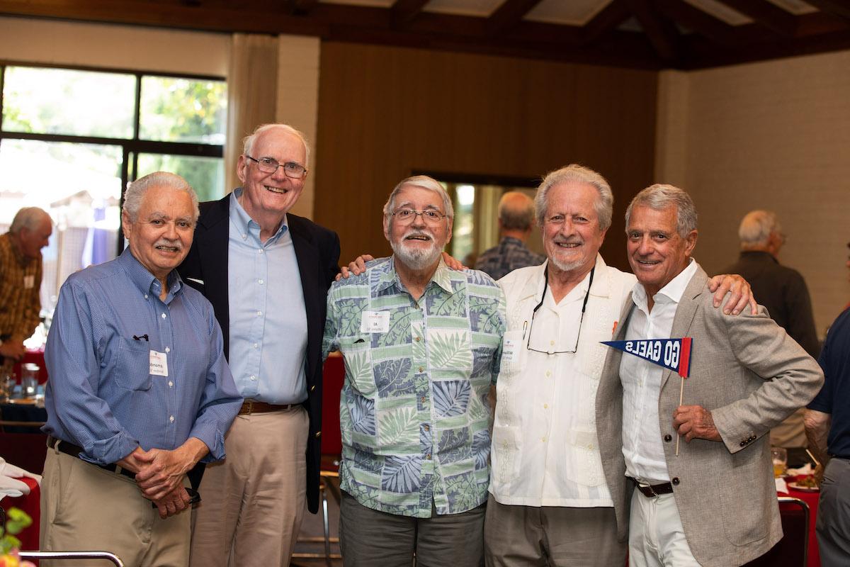 Five alumni smile at the camera, one holding a Go Gaels pennant